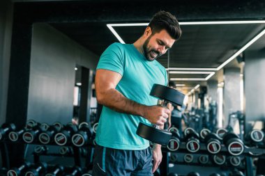 Spor salonunda silah eğitmek için dambıl kullanan zinde bir adam..