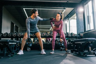 Modern bir spor salonunda birlikte çalışan genç bir adam ve kadın, ağırlık kaldırırken odaklanır ve kararlıdır..