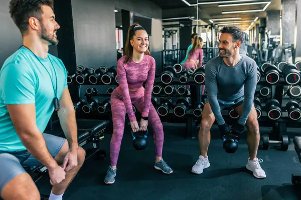 Modern bir spor salonunda iki erkek ve bir kadın ağırlık kaldırıyor.. 