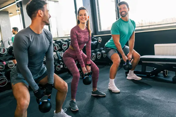 Modern bir spor salonunda iki erkek ve bir kadın ağırlık kaldırıyor.. 