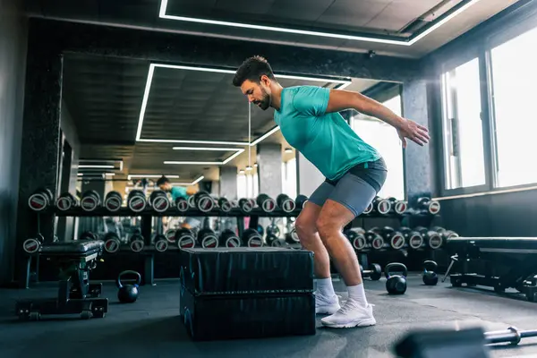 Modern bir spor salonunda yapılan yoğun bir çalışma sırasında zıplarken yakalanan zinde genç bir adam..
