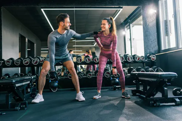 Modern bir spor salonunda birlikte çalışan genç bir adam ve kadın, ağırlık kaldırırken odaklanır ve kararlıdır..