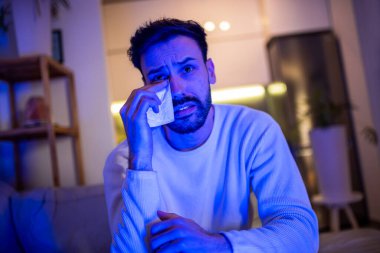 Karanlık odasında tek başına oturan bir adam, televizyon izlerken gözlerinden yaşlar boşalıyor..