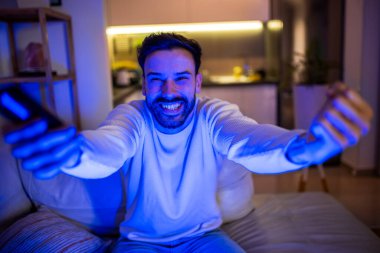 Karanlık bir odada televizyon izleyen neşeli bir adam. Yüzü ekranın yumuşak parıltısıyla aydınlanıyor.. 