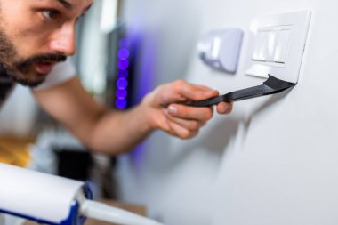 Genç bir tamirci dairede ufak tefek tamiratlar yapıyor. Silikon dolgusunu hassasiyetle uyguluyor..