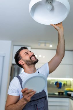 Genç bir tamirci bir dairedeki avizeyi modern bir LED panelle değiştiriyor..