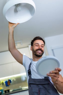 Genç bir tamirci bir dairedeki avizeyi modern bir LED panelle değiştiriyor..
