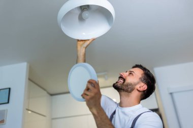 Genç bir tamirci bir dairedeki avizeyi modern bir LED panelle değiştiriyor..