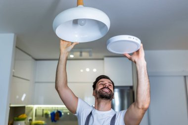 Genç bir tamirci bir dairedeki avizeyi modern bir LED panelle değiştiriyor..