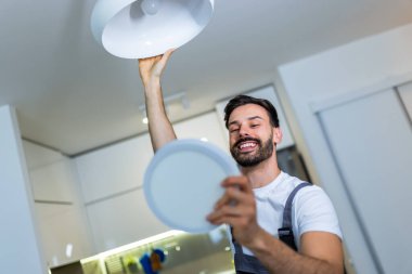 Genç bir tamirci bir dairedeki avizeyi modern bir LED panelle değiştiriyor..