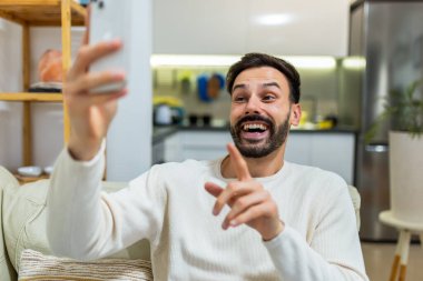 Genç bir adam rahat bir oturma odasında kanepede oturuyor, akıllı telefonuyla bir video görüşmesi yapıyor.. 
