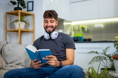 Genç, sakallı bir adam rahat bir şekilde bir kanepede oturur rahat bir oturma odasında, tamamen bir kitaba gömülmüş. Evinin sessizliğiyle çevrili, huzurlu bir yalnızlık anının tadını çıkarıyor, sayfalarla ekran zamanını değiş tokuş ediyor..