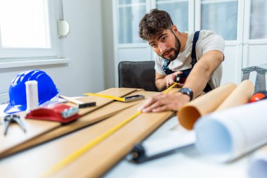 Genç bir adam dairesinin tadilatı için gayretli bir şekilde çalışıyor, lamine döşeme döşemesine odaklanıyor. Elindeki doğru araçlarla, dikkatle ölçer ve plastik panelleri yerine yerleştirir, boşluğu DIY becerileriyle dönüştürür. 