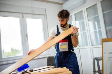 Genç bir adam dairesinin tadilatı için gayretli bir şekilde çalışıyor, lamine döşeme döşemesine odaklanıyor. Elindeki doğru araçlarla, dikkatle ölçer ve plastik panelleri yerine yerleştirir, boşluğu DIY becerileriyle dönüştürür. 