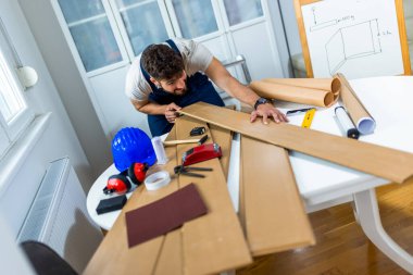 Genç bir adam dairesinin tadilatı için gayretli bir şekilde çalışıyor, lamine döşeme döşemesine odaklanıyor. Elindeki doğru araçlarla, dikkatle ölçer ve plastik panelleri yerine yerleştirir, boşluğu DIY becerileriyle dönüştürür. 