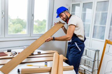 Genç bir adam dairesinin tadilatı için gayretli bir şekilde çalışıyor, lamine döşeme döşemesine odaklanıyor. Elindeki doğru araçlarla, dikkatle ölçer ve plastik panelleri yerine yerleştirir, boşluğu DIY becerileriyle dönüştürür. 