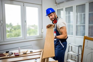 Genç bir adam dairesinin tadilatı için gayretli bir şekilde çalışıyor, lamine döşeme döşemesine odaklanıyor. Elindeki doğru araçlarla, dikkatle ölçer ve plastik panelleri yerine yerleştirir, boşluğu DIY becerileriyle dönüştürür. 