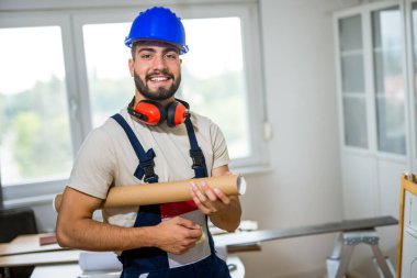 Dairesini yenilemek için özenle çalışan genç bir adamın portresi, lamine döşeme montajına odaklanıyor. Elindeki doğru araçlarla, dikkatlice ölçüyor ve plastik panelleri yerine yerleştiriyor, boşluğu DIY ile dönüştürüyor. 