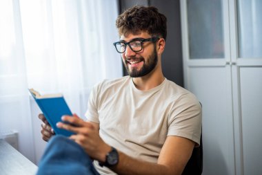 Genç öğrenci elinde bir kitapla rahatça oturur, kendini okumaya verirken gözlük takar. Onun derin konsantrasyonu ve düşünceli ifadesi öğrenme ve genişletme sevincini vurguluyor..