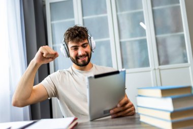 Genç öğrenci kulaklık takarken bir tablet kullanarak çalışmalarına daldı. İster konferans dinlesin, ister eğitim videoları izlesin, ister çevrimiçi araştırmalara odaklansın, o tamamen dijital öğrenme deneyimiyle meşgul..