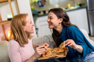 En iyi iki arkadaş oturma odasında sıcak ve eğlenceli bir gece geçiriyorlar, pizza dilimleri ve kırmızı şarabın tadını çıkarıyorlar. Kahkahalar, rahat giysiler içinde rahatlarken, hikayelerini paylaşırken ve anılar yaratırken alanı dolduruyor.. 