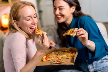 En iyi iki arkadaş oturma odasında sıcak ve eğlenceli bir gece geçiriyorlar, pizza dilimleri ve kırmızı şarabın tadını çıkarıyorlar. Kahkahalar, rahat giysiler içinde rahatlarken, hikayelerini paylaşırken ve anılar yaratırken alanı dolduruyor.. 
