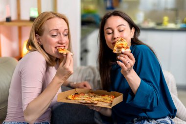 En iyi iki arkadaş oturma odasında sıcak ve eğlenceli bir gece geçiriyorlar, pizza dilimleri ve kırmızı şarabın tadını çıkarıyorlar. Kahkahalar, rahat giysiler içinde rahatlarken, hikayelerini paylaşırken ve anılar yaratırken alanı dolduruyor.. 