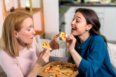 En iyi iki arkadaş oturma odasında sıcak ve eğlenceli bir gece geçiriyorlar, pizza dilimleri ve kırmızı şarabın tadını çıkarıyorlar. Kahkahalar, rahat giysiler içinde rahatlarken, hikayelerini paylaşırken ve anılar yaratırken alanı dolduruyor.. 