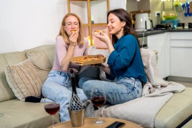 En iyi iki arkadaş oturma odasında sıcak ve eğlenceli bir gece geçiriyorlar, pizza dilimleri ve kırmızı şarabın tadını çıkarıyorlar. Kahkahalar, rahat giysiler içinde rahatlarken, hikayelerini paylaşırken ve anılar yaratırken alanı dolduruyor.. 