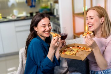 En iyi iki arkadaş oturma odasında sıcak ve eğlenceli bir gece geçiriyorlar, pizza dilimleri ve kırmızı şarabın tadını çıkarıyorlar. Kahkahalar, rahat giysiler içinde rahatlarken, hikayelerini paylaşırken ve anılar yaratırken alanı dolduruyor.. 