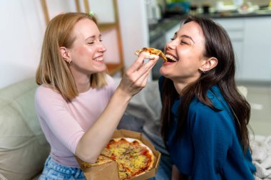 En iyi iki arkadaş sıcak bir gece geçiriyorlar, oturma odasında pizzanın tadını çıkarıyorlar. Tatlı ve eğlenceli bir jestle, biri diğerini bir dilimle besliyor, özen, kahkaha ve sıcaklık dolu bir an yaratıyor. Bu...