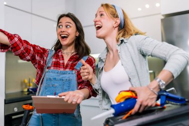 İki kız ellerinde aletlerle bir odada duruyorlar. Evi tamir etmeye ve yenilemeye hazırlar..