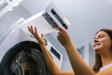 Genç bir kız çamaşır kurutma makinesinden su kabını çıkarıyor. Makinenin iyi çalışması için düzenli bakım yapıyor..