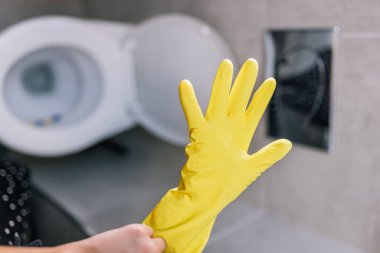 Lastik temizleme eldiveni takan, tuvaleti temizlemeye hazırlanan genç bir kızın yakın çekim görüntüsü.. 