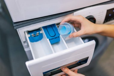 Kadın çamaşır makinesine yumuşatıcı koyar..