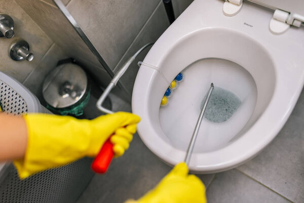 A young woman using drain cleaner to unclog a toilet bowl.