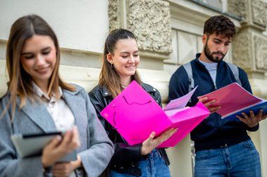 Üç öğrenci serbest bir ortamda oturuyorlar, her biri aynı yeri paylaşırken kendi derslerine odaklanıyor. Toplumsal bir ortamda bağımsız öğrenmeyi vurgulayan kitaplar, notlar veya tabletler tutuyorlar.. 