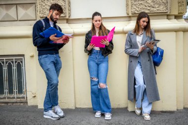 Üç öğrenci serbest bir ortamda oturuyorlar, her biri aynı yeri paylaşırken kendi derslerine odaklanıyor. Toplumsal bir ortamda bağımsız öğrenmeyi vurgulayan kitaplar, notlar veya tabletler tutuyorlar.. 