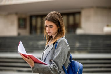 Güneşli bir günde dışarıda durmuş kitap okuyan genç bir kız öğrenci. Odaklanmış ve derslerine dalmış durumda..