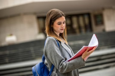 Güneşli bir günde dışarıda durmuş kitap okuyan genç bir kız öğrenci. Odaklanmış ve derslerine dalmış durumda..