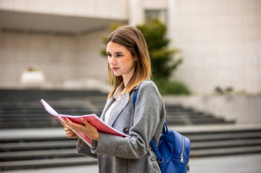 Güneşli bir günde dışarıda durmuş kitap okuyan genç bir kız öğrenci. Odaklanmış ve derslerine dalmış durumda..