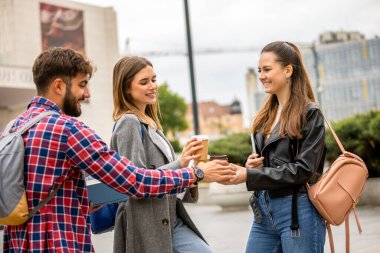 Güneşli bir günde üç üniversite öğrencisi dışarıda birlikte çalışıyor. Bir öğrenci kahve getirdi, çalışma seansına gelişigüzel bir dokunuş ekledi..