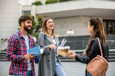 Güneşli bir günde üç üniversite öğrencisi dışarıda birlikte çalışıyor. Bir öğrenci kahve getirdi, çalışma seansına gelişigüzel bir dokunuş ekledi..