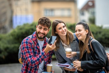 Üç öğrenci dışarıda toplanmış, akıllı telefondan bir sesli mesaj dinliyorlar.. 