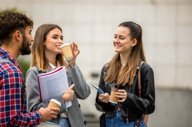 Güneşli bir günde üç üniversite öğrencisi dışarıda birlikte çalışıyor. Bir öğrenci kahve getirdi, çalışma seansına gelişigüzel bir dokunuş ekledi..
