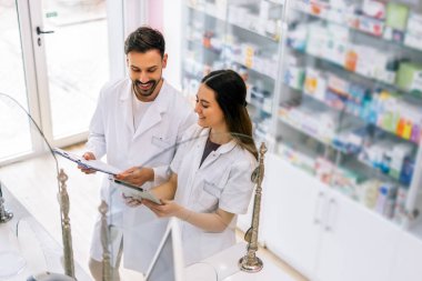 Eczane tezgahının arkasında duran iki profesyonel eczacı dikkatle ilaç kutusuna bakıyor.. 