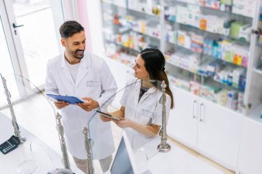 Eczane tezgahının arkasında duran iki profesyonel eczacı dikkatle ilaç kutusuna bakıyor.. 
