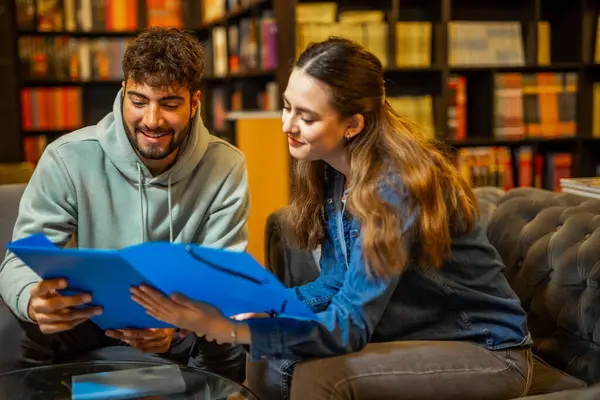 İki odaklanmış öğrenci sessiz bir kütüphane ortamında birlikte okuyorlar, bir klasörden içeriği okuyup tartışıyorlar.. 