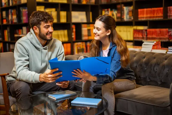 İki odaklanmış öğrenci sessiz bir kütüphane ortamında birlikte okuyorlar, bir klasörden içeriği okuyup tartışıyorlar.. 