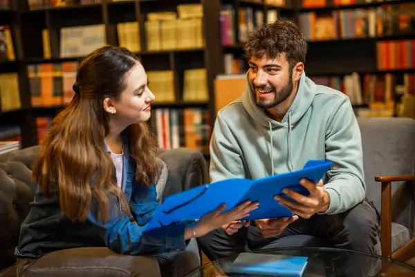 İki odaklanmış öğrenci sessiz bir kütüphane ortamında birlikte okuyorlar, bir klasörden içeriği okuyup tartışıyorlar.. 